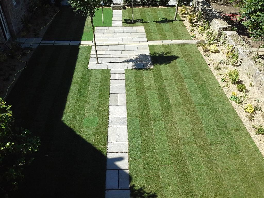 Pelouse à l'arrière avec un étroit chemin de pierre menant à une terrasse, bordée de parterres de fleurs et de haies.