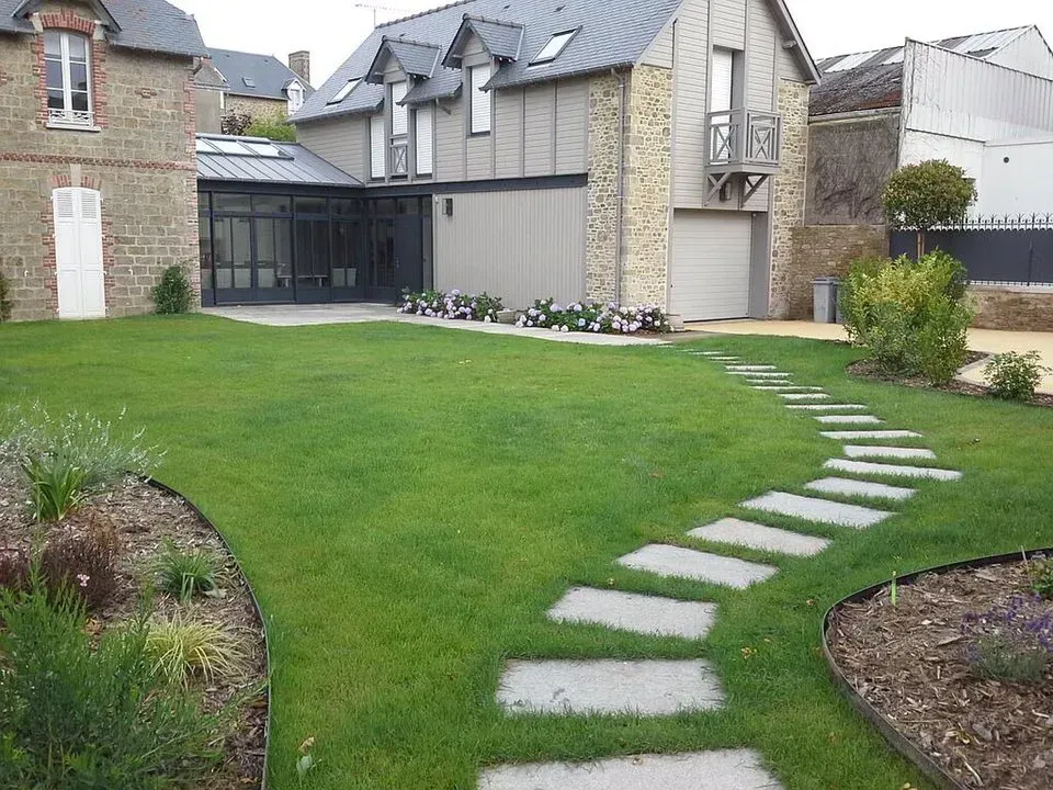 Maison moderne avec pelouse verte et chemin de dalles incurvé.