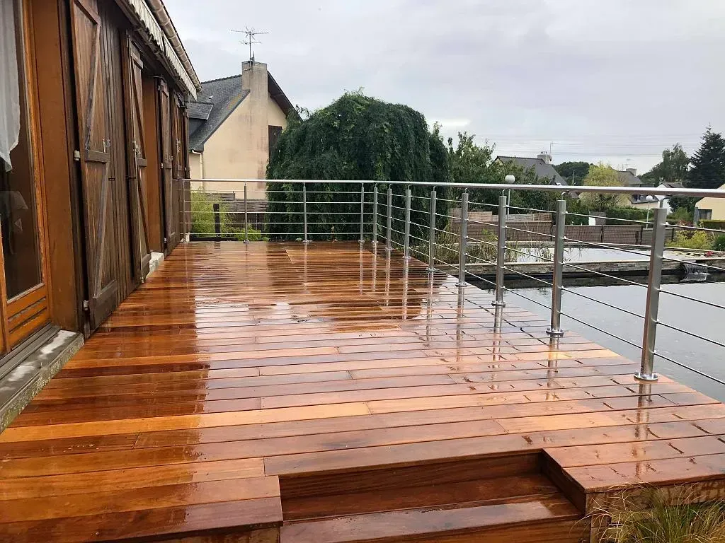 Terrasse en bois sur le toit, avec carrelage brillant, rambarde en métal et petite marche, donnant sur les maisons et les arbres.