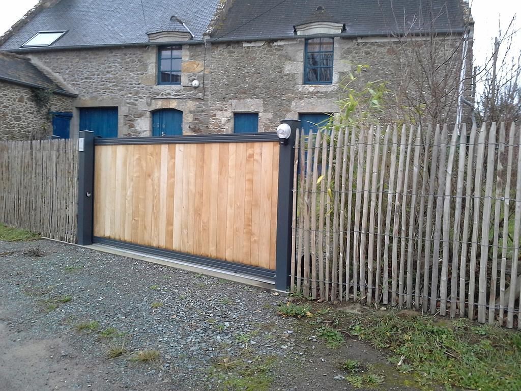 Maison en pierre avec un portail en bois et une clôture patinée par le temps, le long d'une allée de gravier.