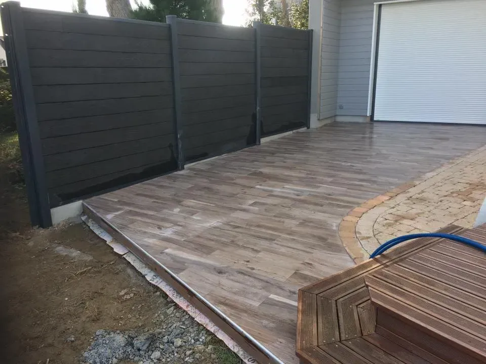 Rampe d'accès en bois à côté d'une allée, bordée d'une clôture sombre et d'une cour sablonneuse.