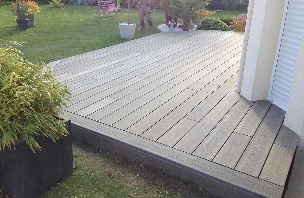 Terrasse en bois à l'arrière de la maison, avec des marches et des arbustes en pot à proximité.