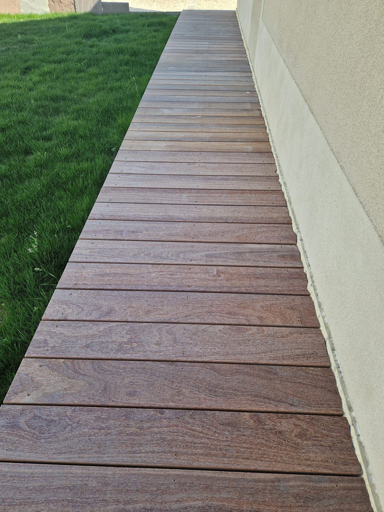 Passerelle en bois longeant un bâtiment beige, bordée de pelouse verte.