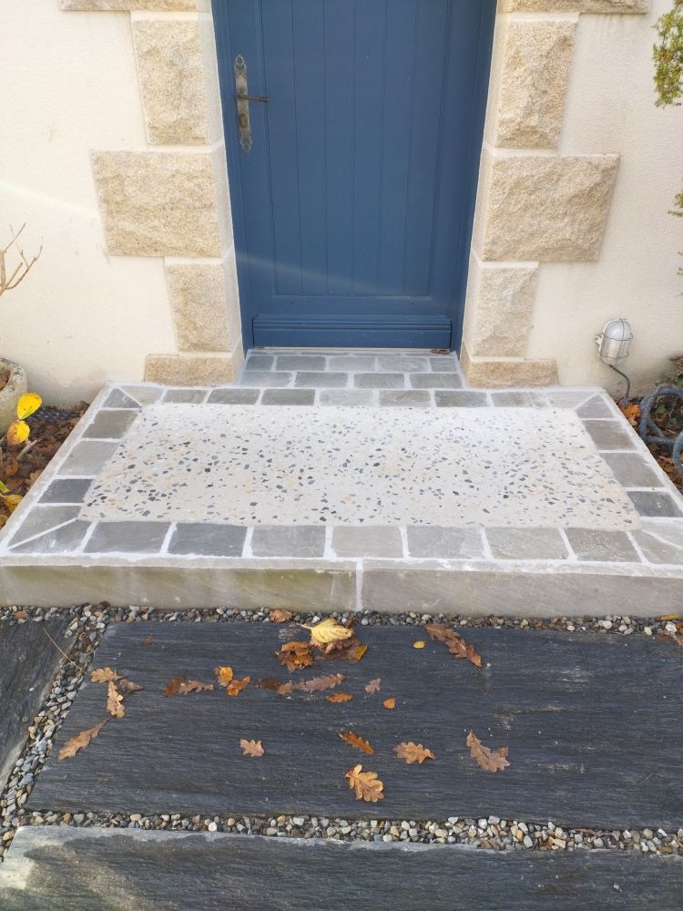 Porte d'entrée bleue avec une petite rampe carrelée et un tapis de seuil en caoutchouc noir y menant.