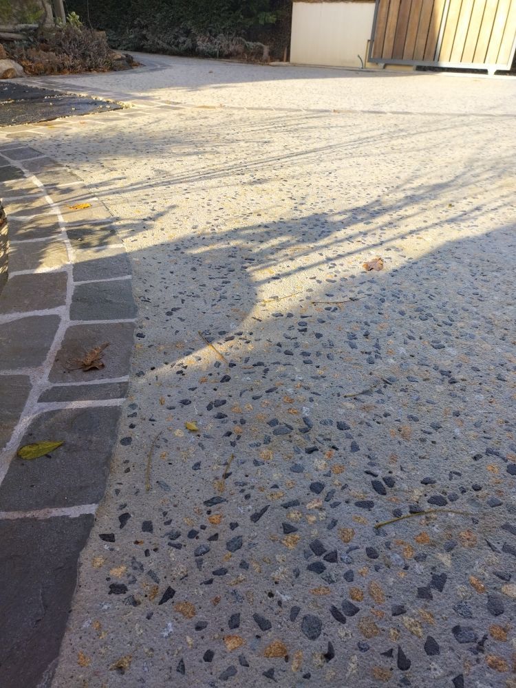 Allée et chemin piétonnier en béton, projetant de longues ombres sur une cour ensoleillée près d'un portail.