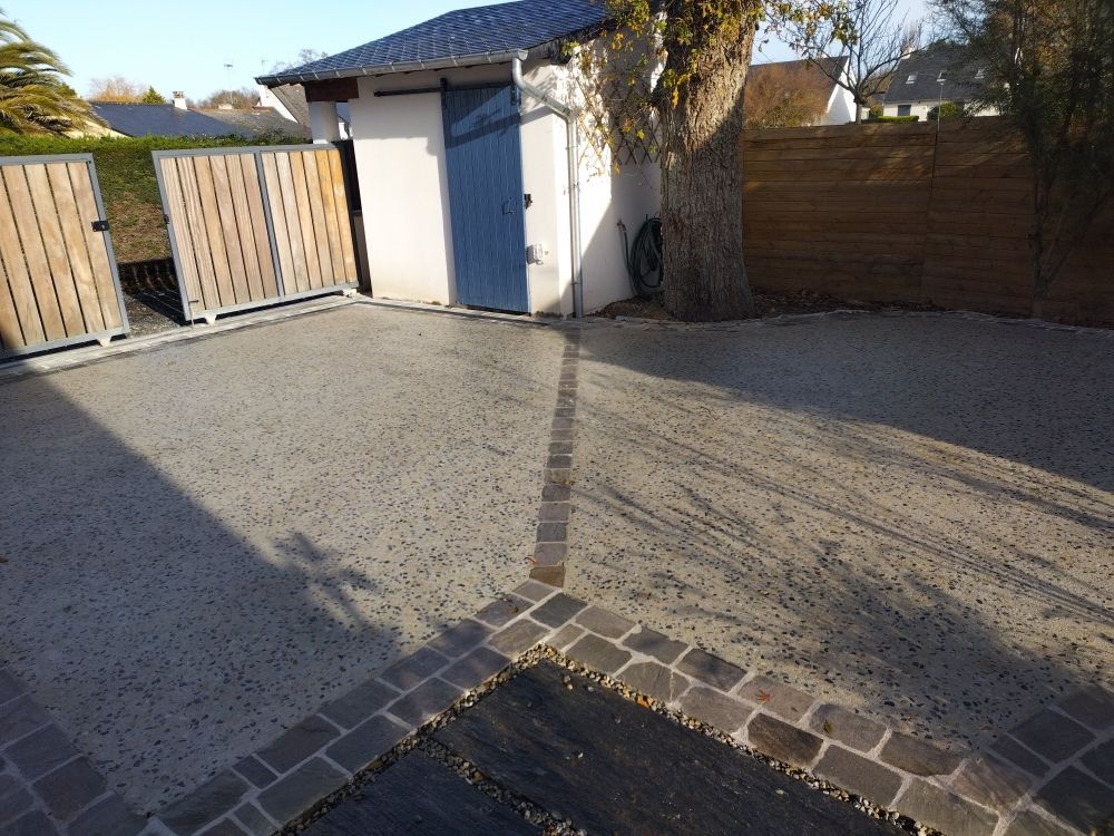 Allée de gravier à l'arrière de la maison avec bordure en pierre, abri de jardin bleu et portail en bois au soleil.