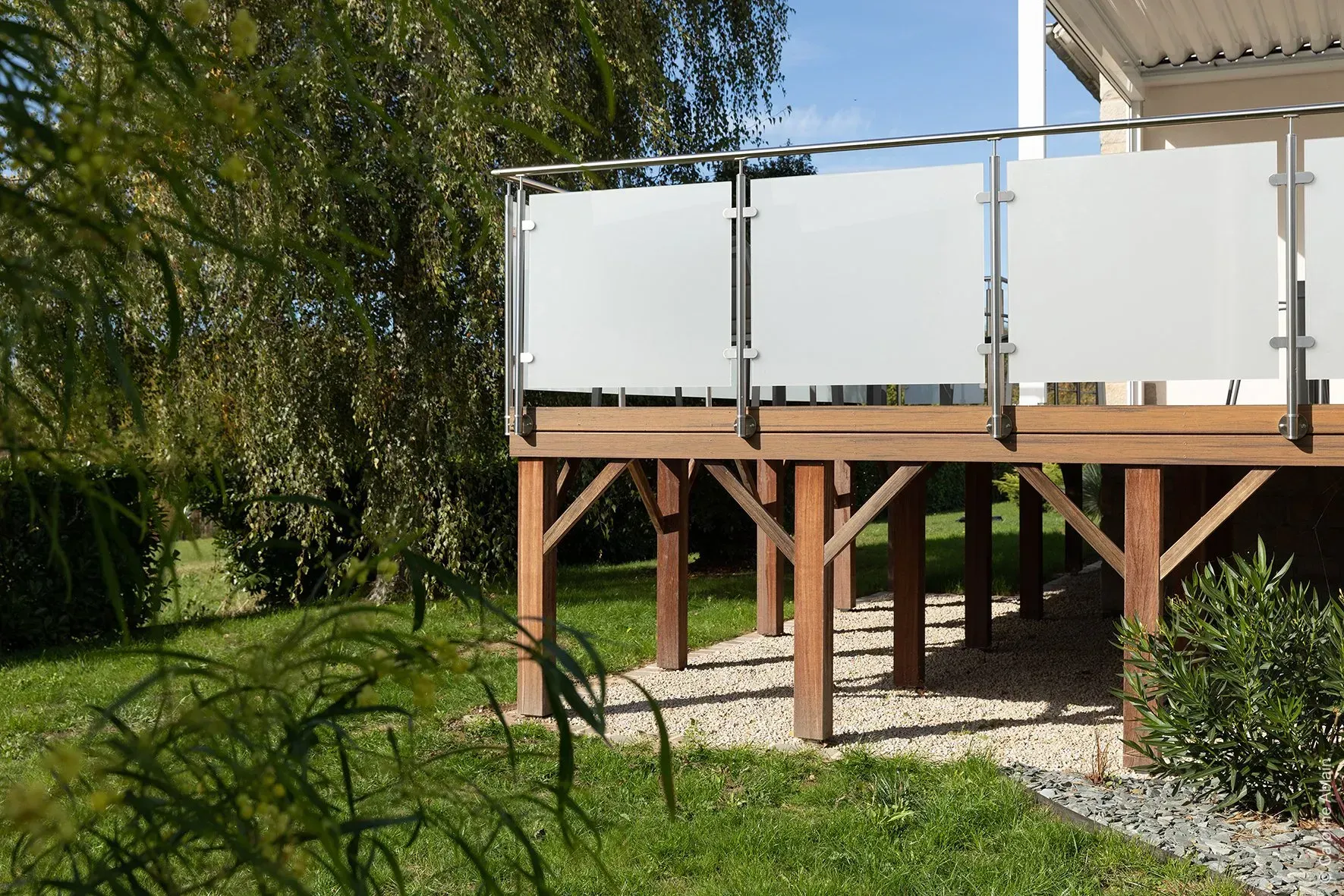 Terrasse surélevée avec panneaux d'intimité blancs et poteaux en bois donnant sur une pelouse sous un ciel bleu azur.