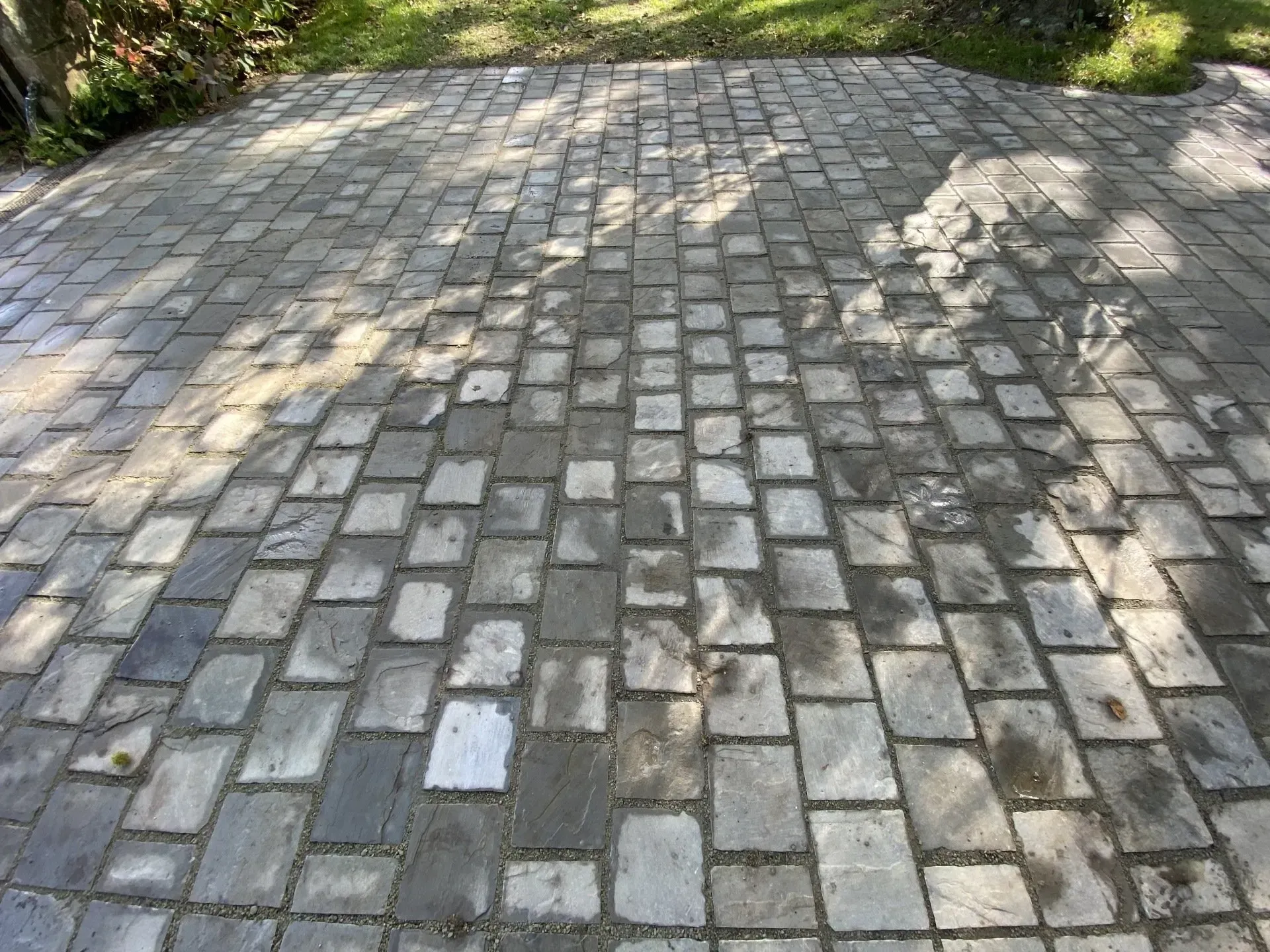 Allée pavée de dalles grises irrégulières, ombrée par les arbres voisins et jouant avec le soleil.