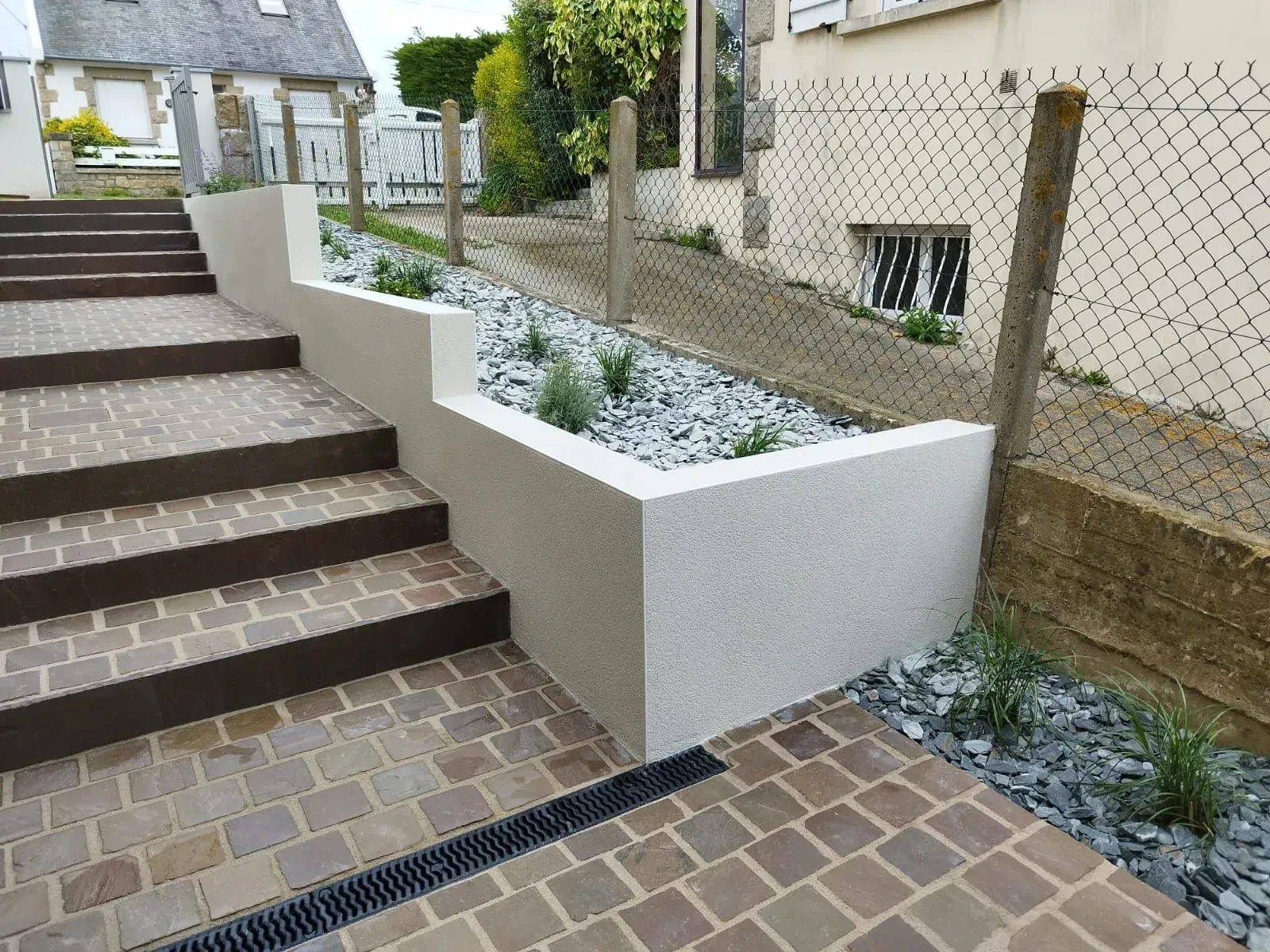 Escalier extérieur à côté d'une jardinière surélevée blanche remplie de gravier et d'une clôture en grillage.