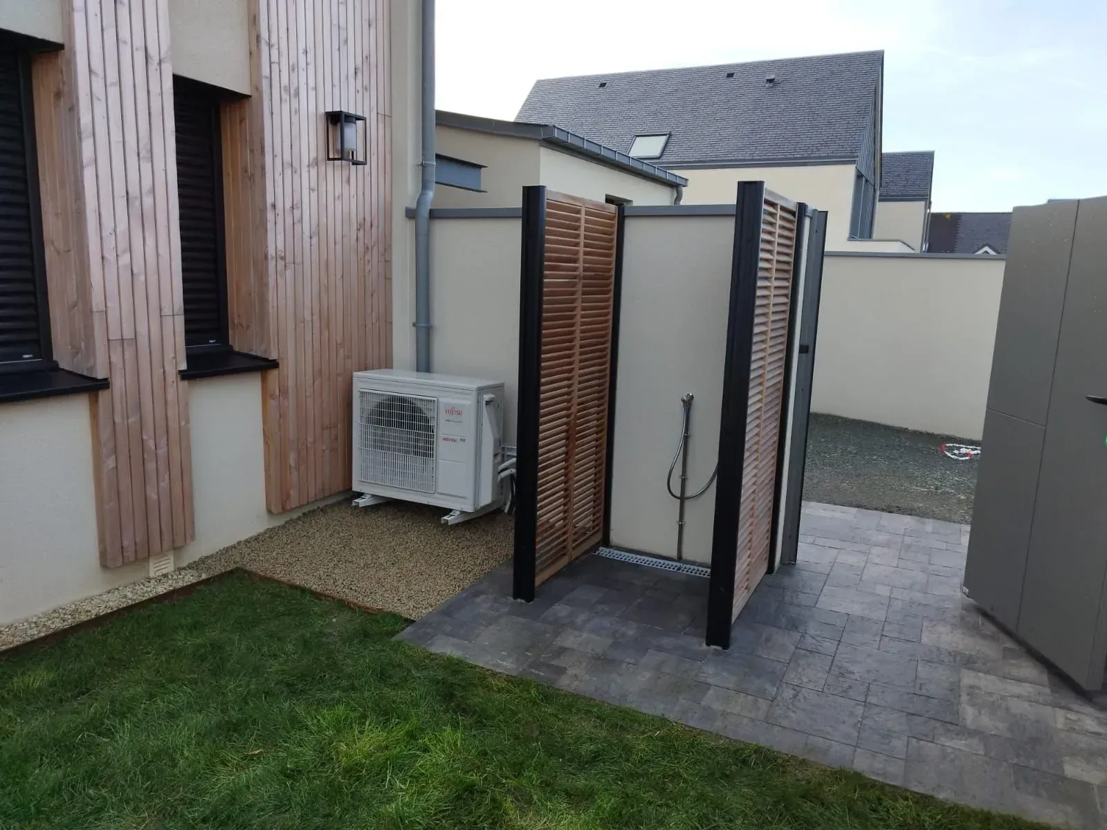 Douche extérieure avec parois en bois pour plus d'intimité, sol carrelé et climatiseur mural à proximité.