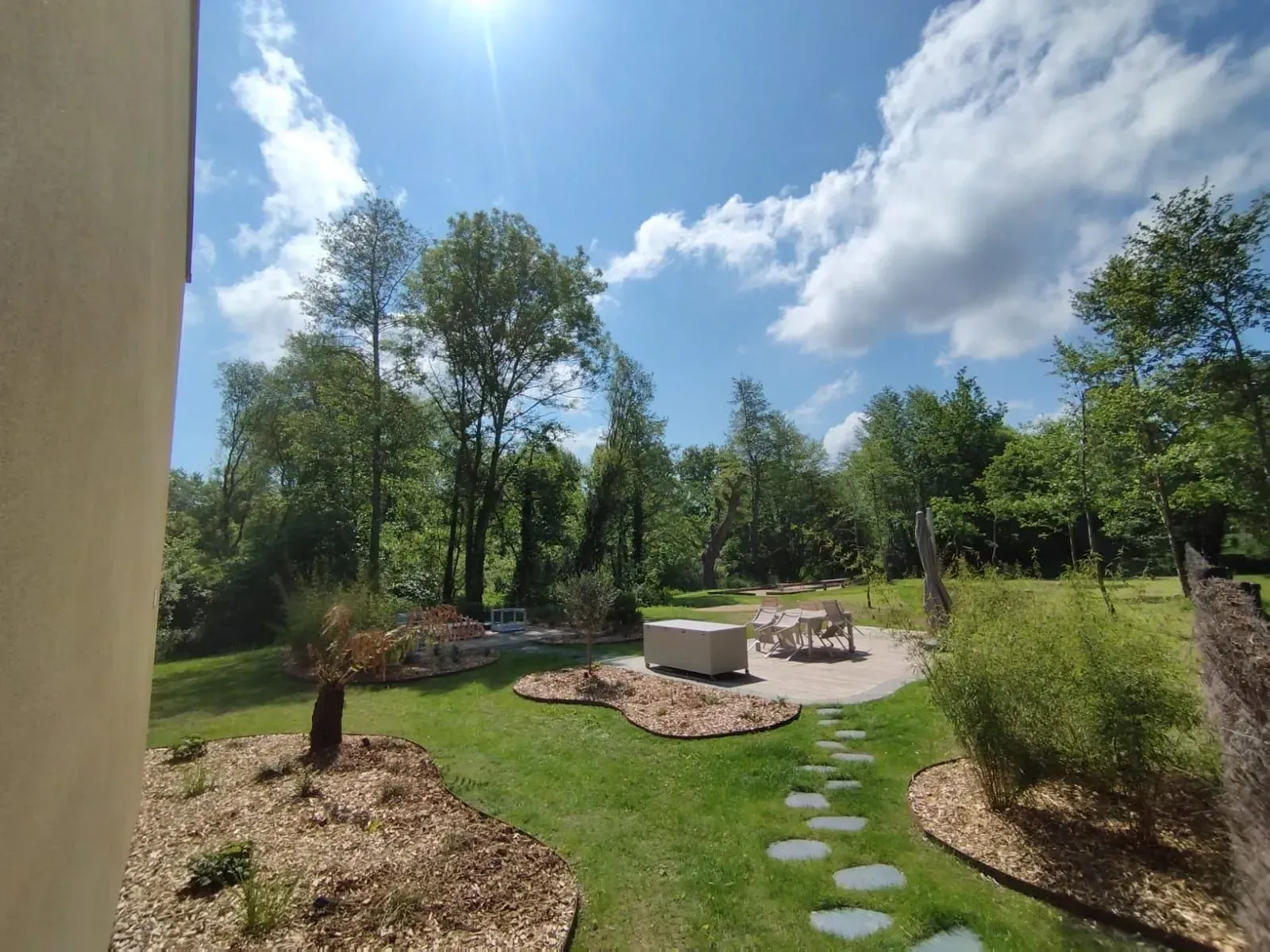 Patio ensoleillé dans la cour arrière avec chemin de pierre, coin salon et arbres sous un ciel bleu.