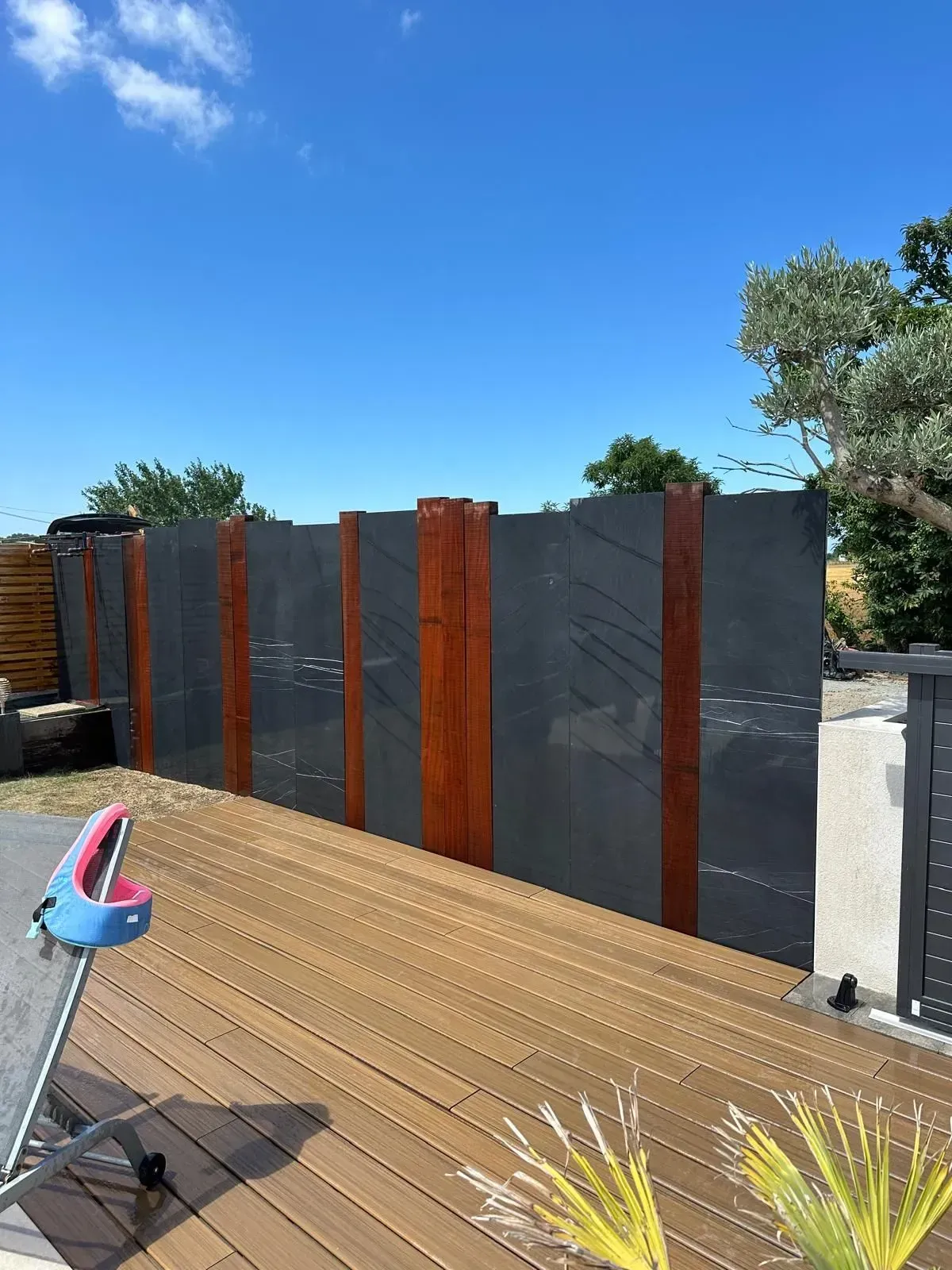 Cour intérieure d'une maison moderne au crépuscule, avec piscine éclairée, terrasse et branches d'olivier au premier plan.