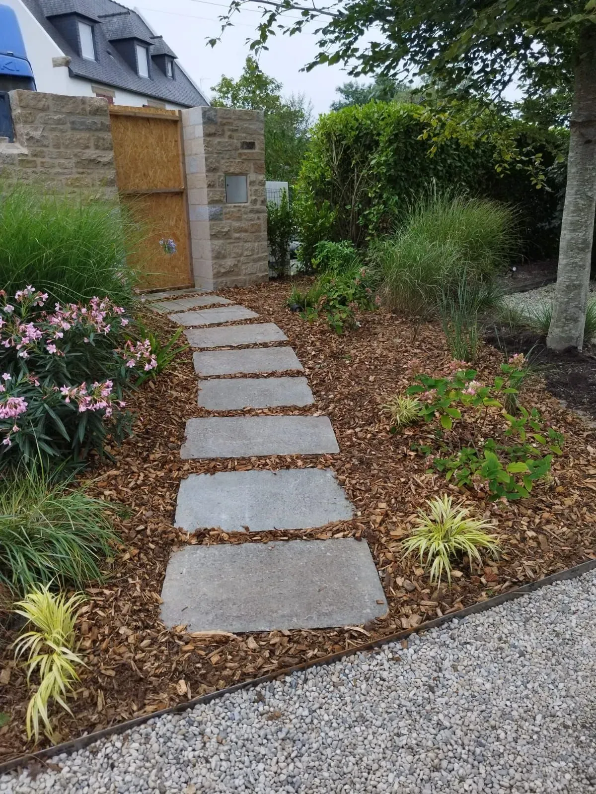 Chemin de dalles traversant un jardin paysager menant à un portail en pierre et à une porte condamnée.