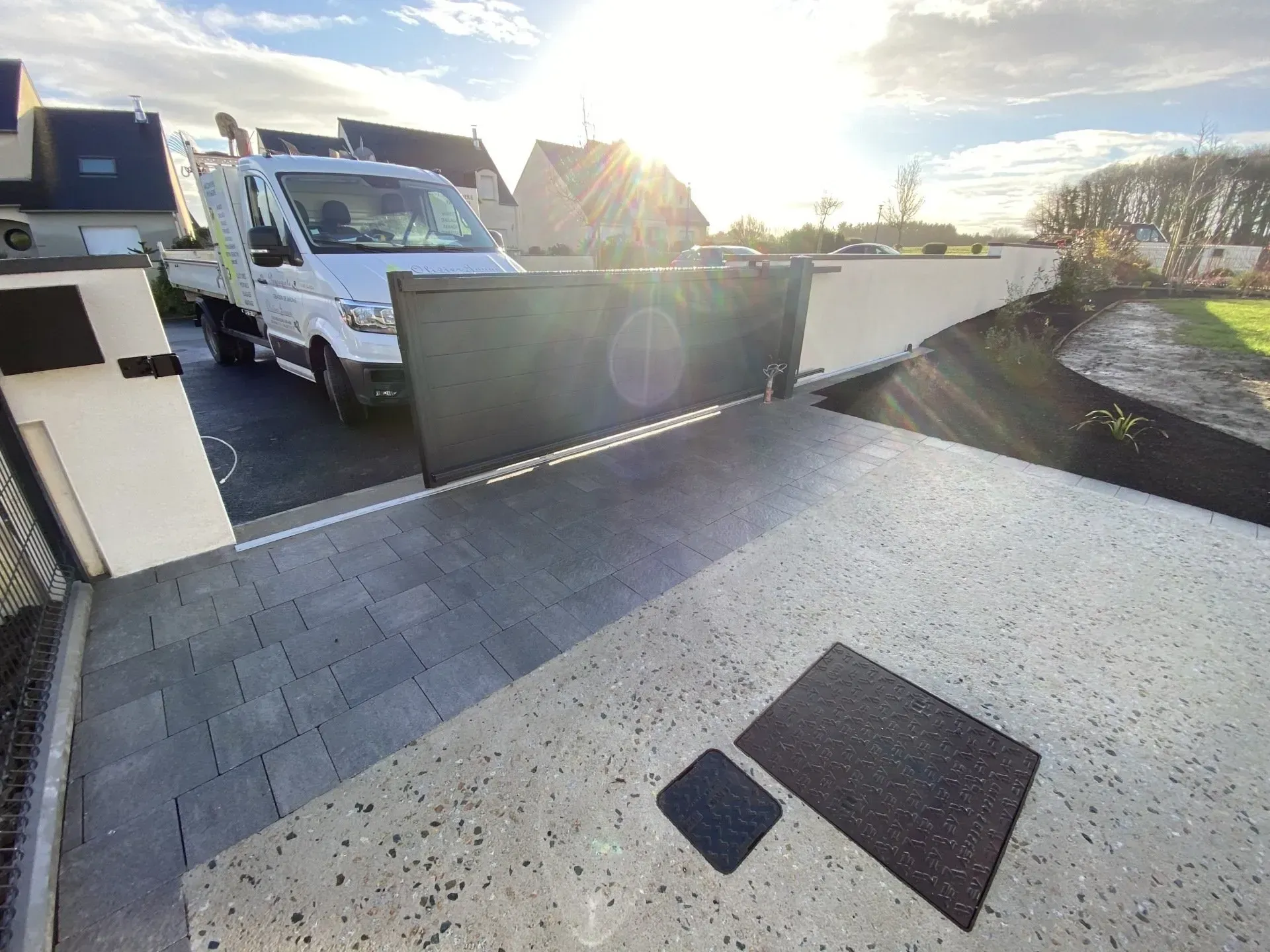 Toit-terrasse avec une camionnette blanche, une barrière verte et des surfaces de gravier baignées de soleil.