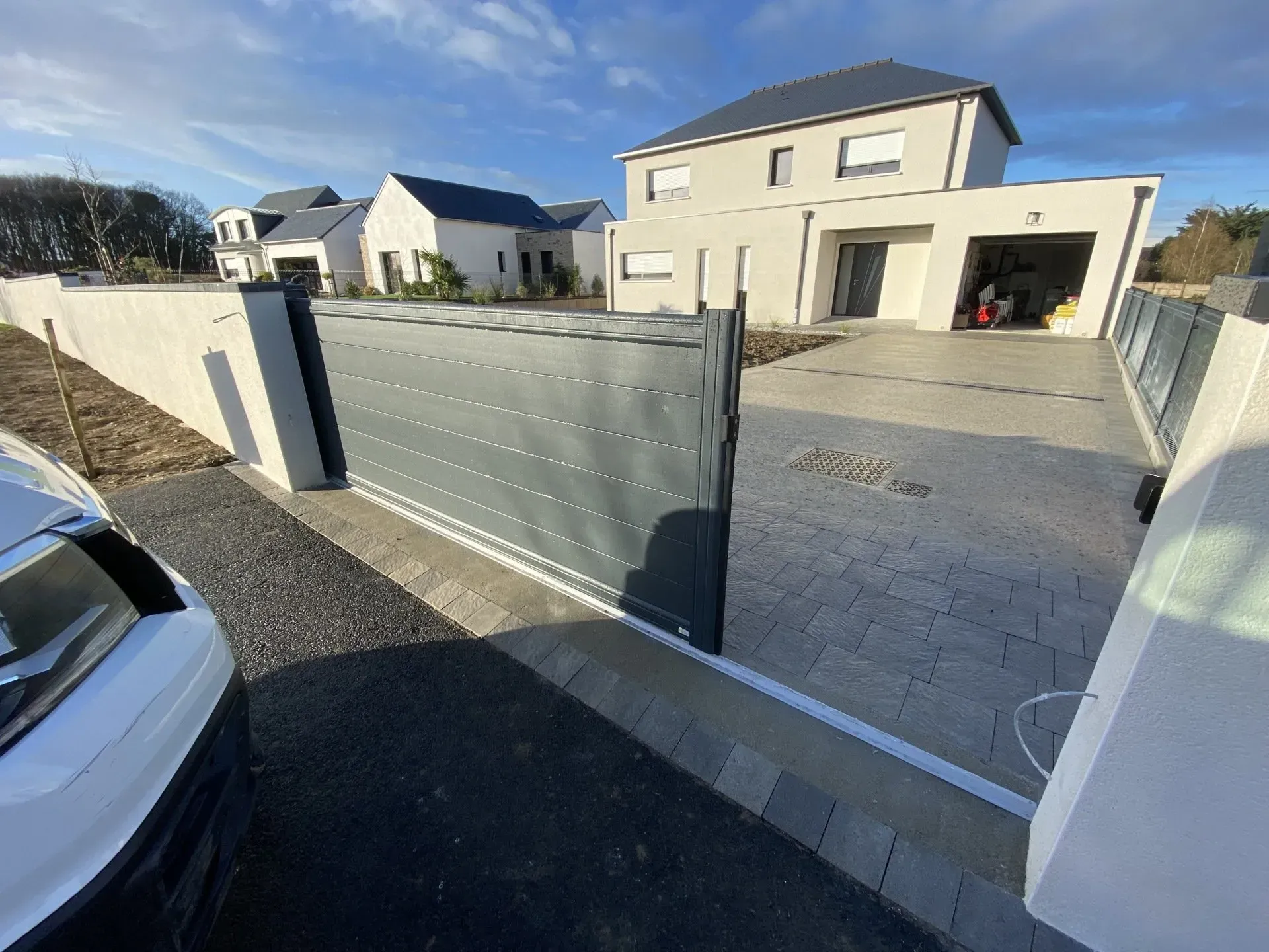 Maison moderne avec une large allée et un portail métallique ouvert, visible depuis la rue.