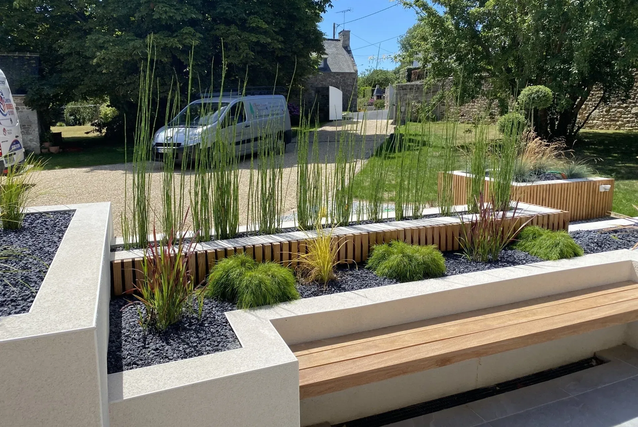 Jardin paysager moderne avec jardinières blanches surélevées, hautes herbes, arbustes et bancs en bois ensoleillés.