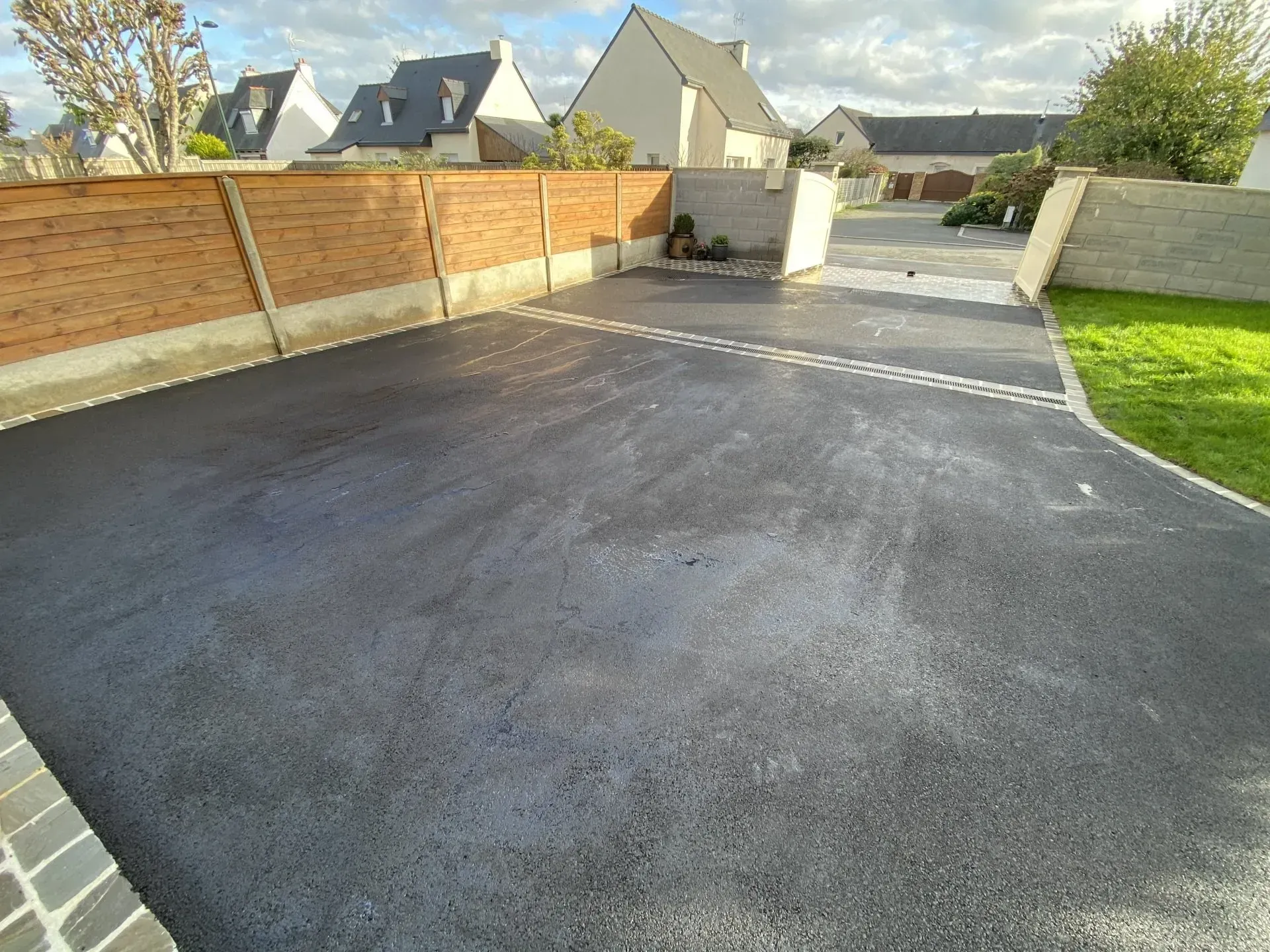 Allée pavée vide longeant un mur de briques et des maisons modernes dans un quartier résidentiel.