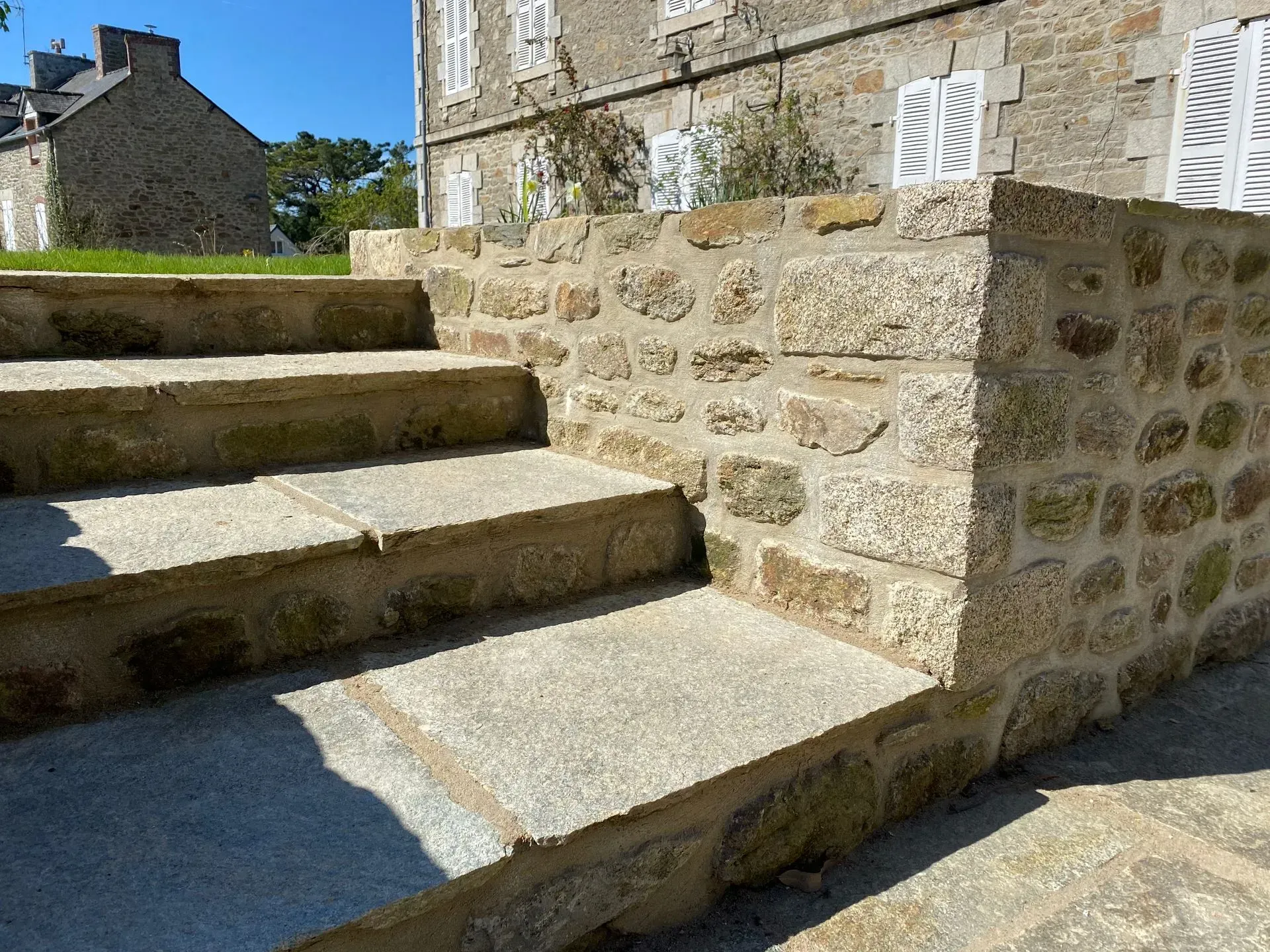 Des marches en pierre longent un mur de pierre baigné de soleil dans une cour extérieure.