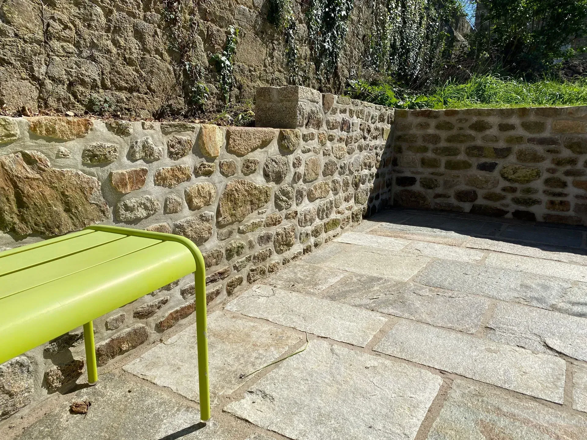 Terrasse en pierre avec murets et banc vert vif au soleil.