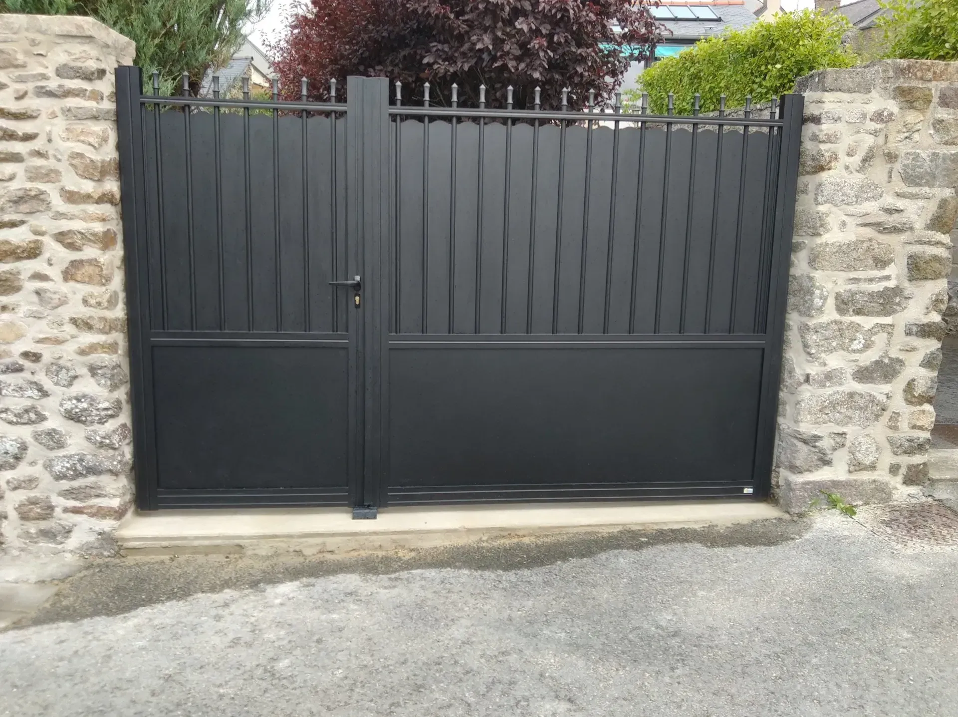 Portail en métal noir entre des murs en pierre à l'entrée d'une allée.