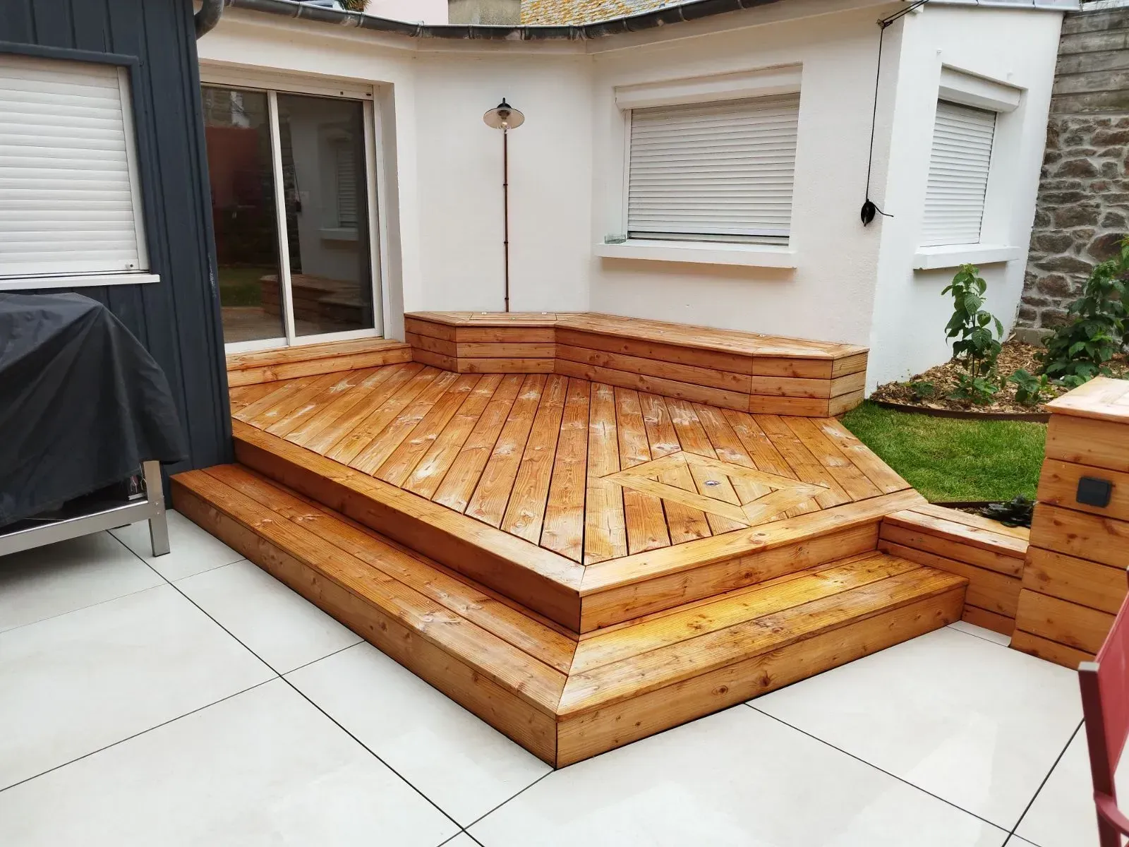 Terrasse en bois avec marches jouxtant le patio d'une maison blanche et une porte-fenêtre coulissante.