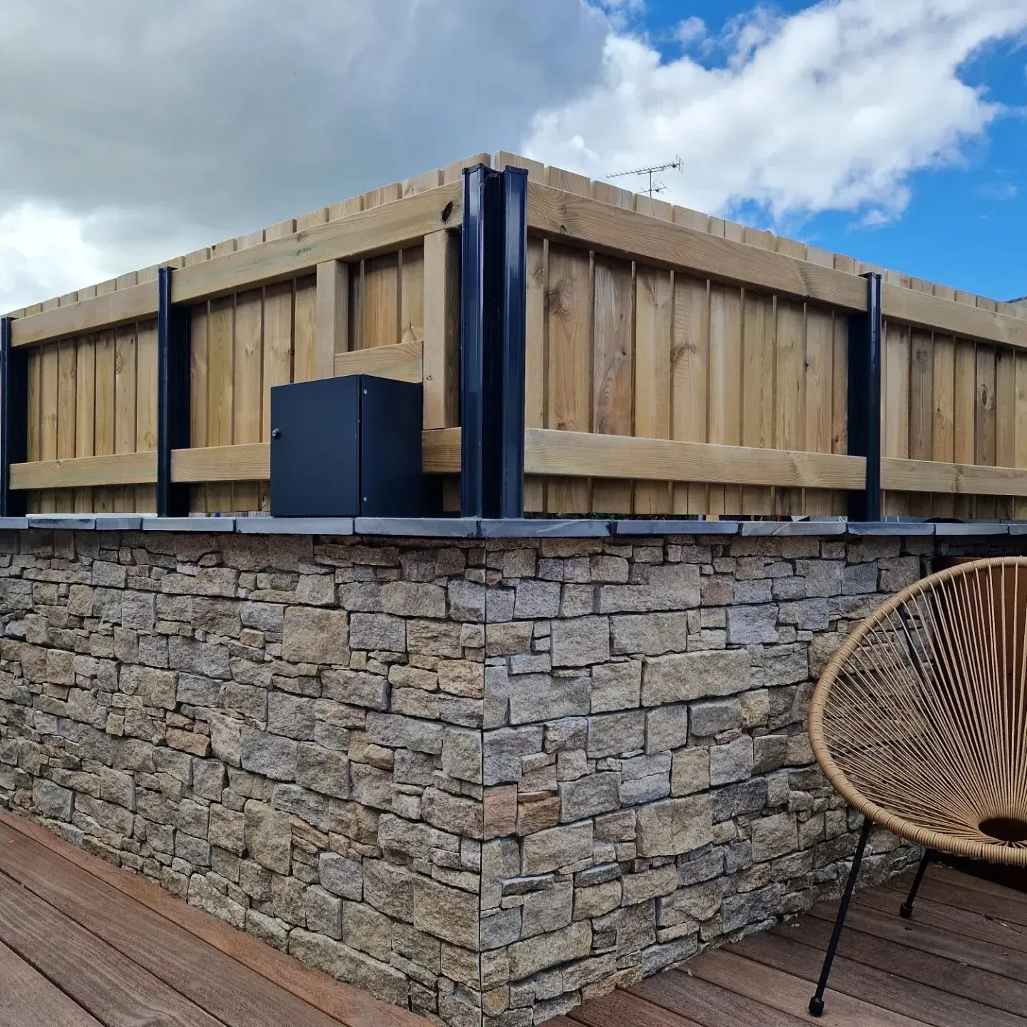Bar extérieur en pierre avec balustrade en bois et ciel bleu au-dessus, à côté d'une chaise en osier et d'une terrasse.
