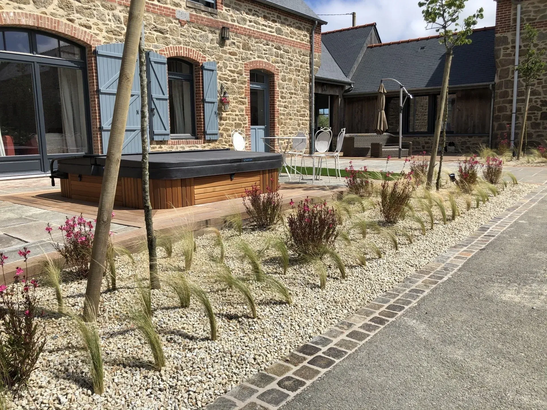 Cour en briques avec parterres de gravier, petits arbustes et un bâtiment en pierre avec de grandes fenêtres.