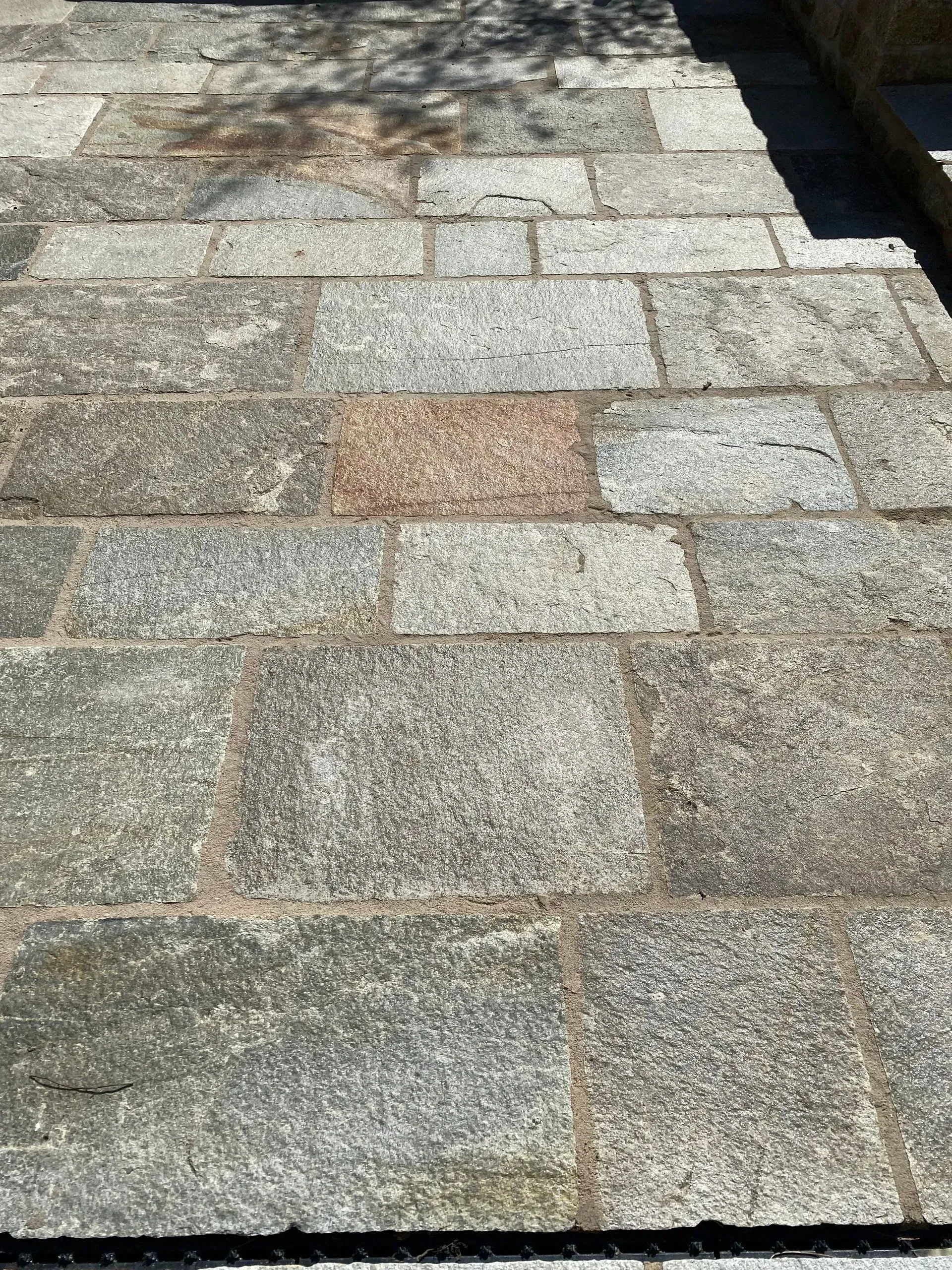 Allée en pierre avec des dalles rectangulaires et un carré de pierres rougeâtres au centre.