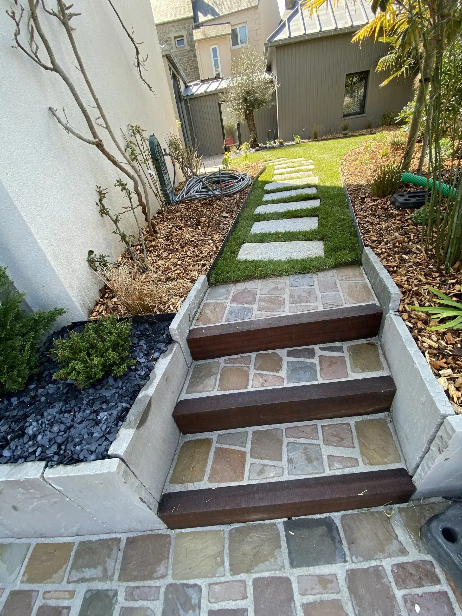 Un escalier d'entrée mène à un chemin paysager dans la cour arrière, agrémenté de dalles de pierre et de parterres de gravier.