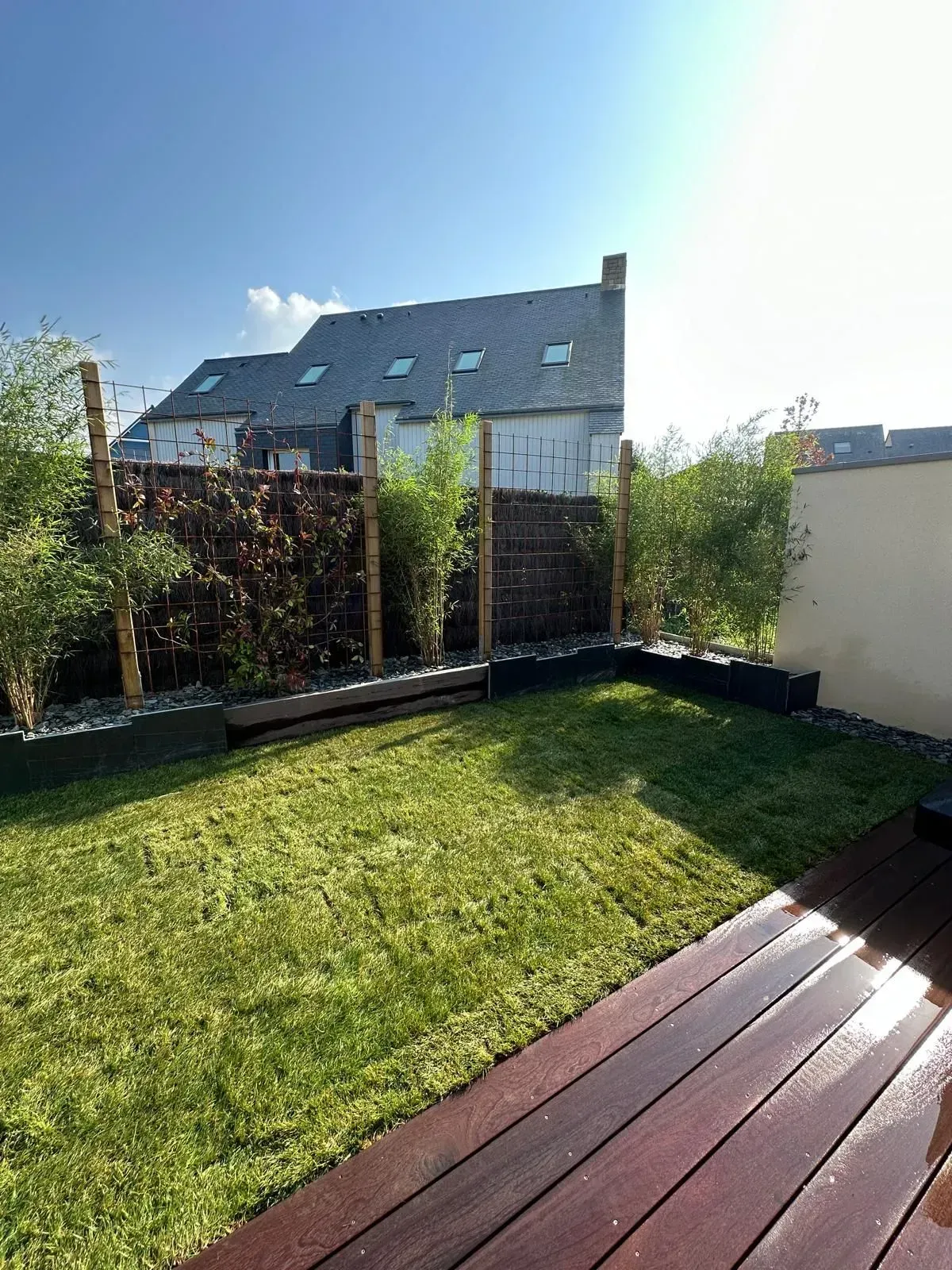 Cour arrière avec pelouse verte, terrasse en bois et haute clôture assurant l'intimité, baignée de soleil.