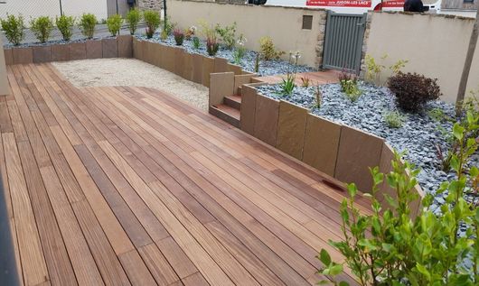 Terrasse en bois dans une cour paysagée avec jardinières surélevées et bordure de gravier, vue d'en haut.