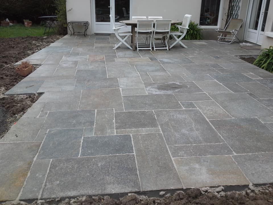 Terrasse en pierre avec table et chaises d'extérieur devant une maison.