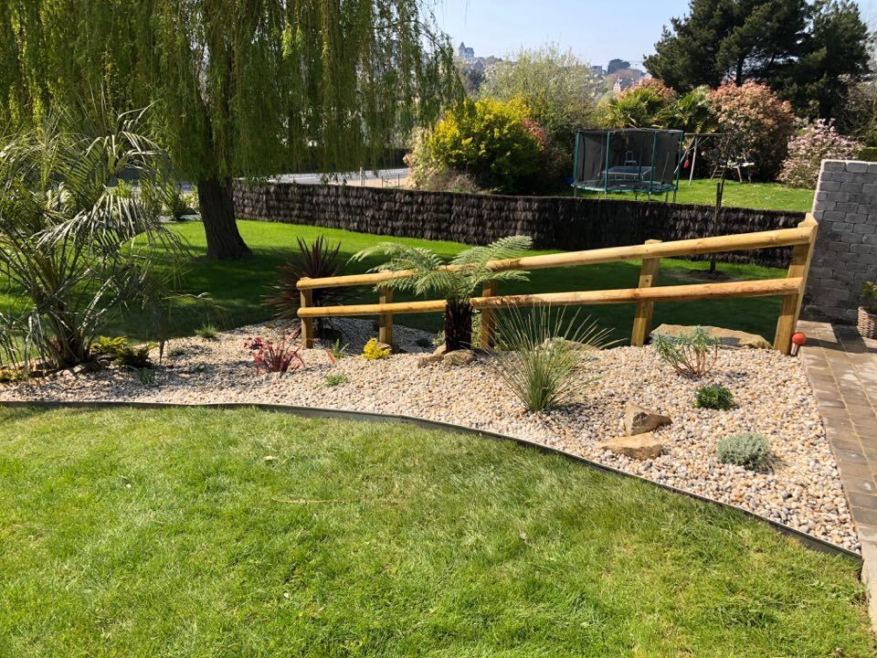 Jardin arrière avec une clôture en bois, une pelouse verte et des plantes aménagées au bord d'un étang.