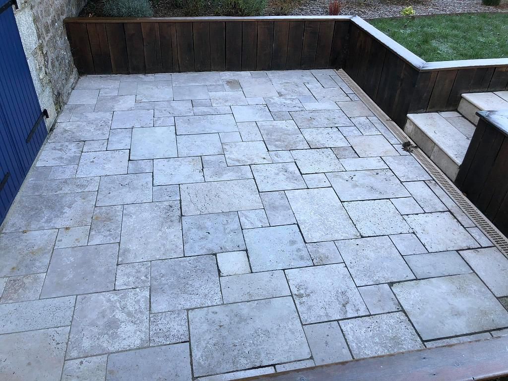 Terrasse carrelée en pierre avec bordures de jardinières surélevées en bois et une petite marche sur la droite.