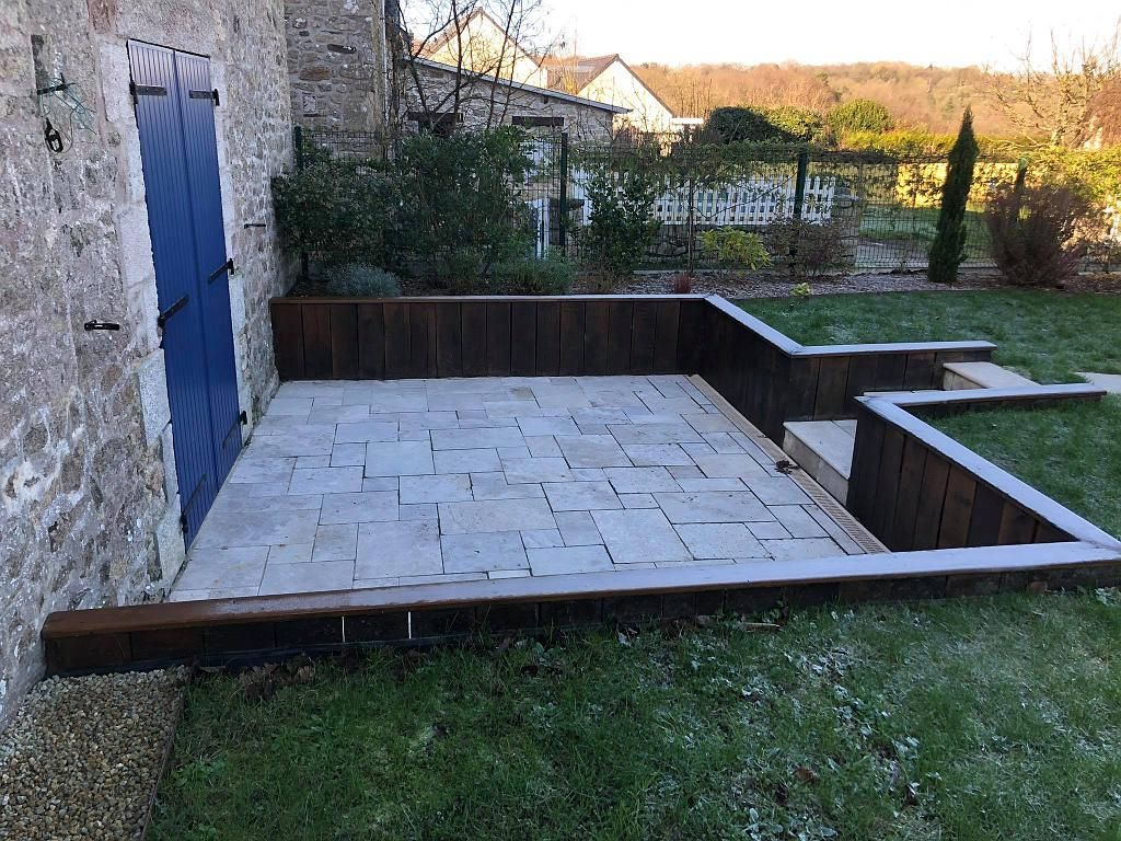 Terrasse en pierre et marches donnant sur un jardin avec pelouse, murets et une porte bleue sur la gauche.