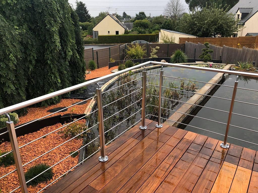 Balcon en bois avec rambarde en acier inoxydable donnant sur un jardin paysager et les maisons du quartier.