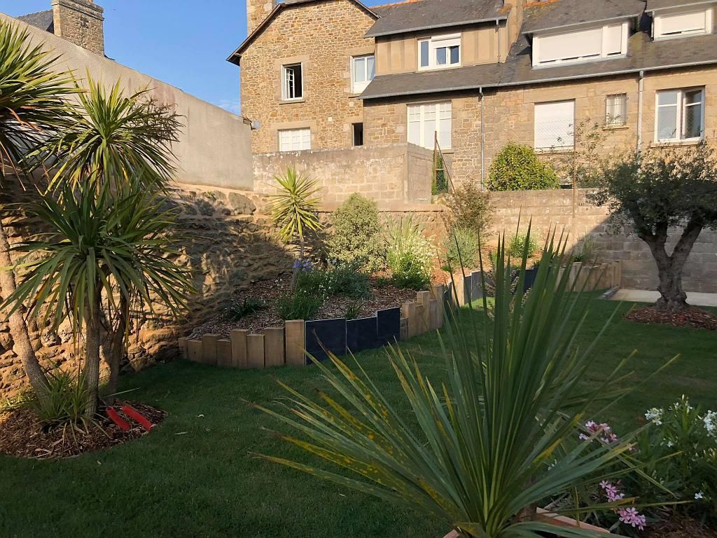 Cour intérieure avec palmiers et fleurs devant une maison en pierre par une journée ensoleillée.