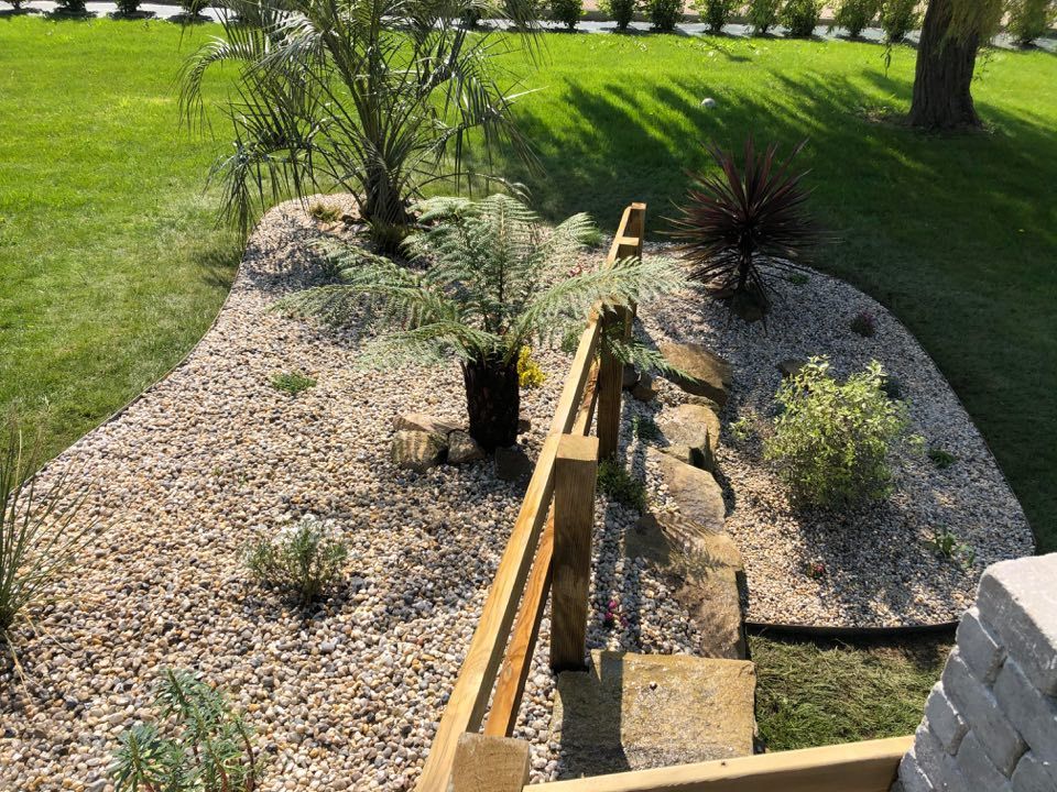 Jardinière surélevée avec quelques plantes éparses et du gravier dans une cour gazonnée, vue du dessus.