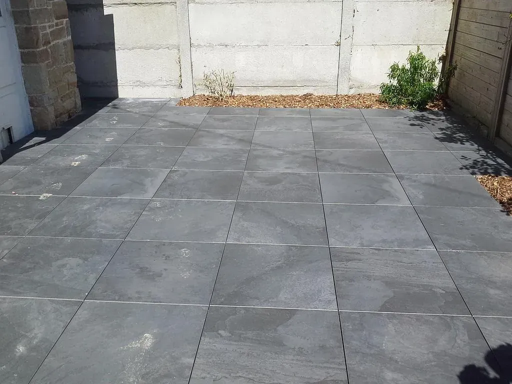 Petite cour pavée avec des carreaux gris entre des murs en béton et une porte de garage.