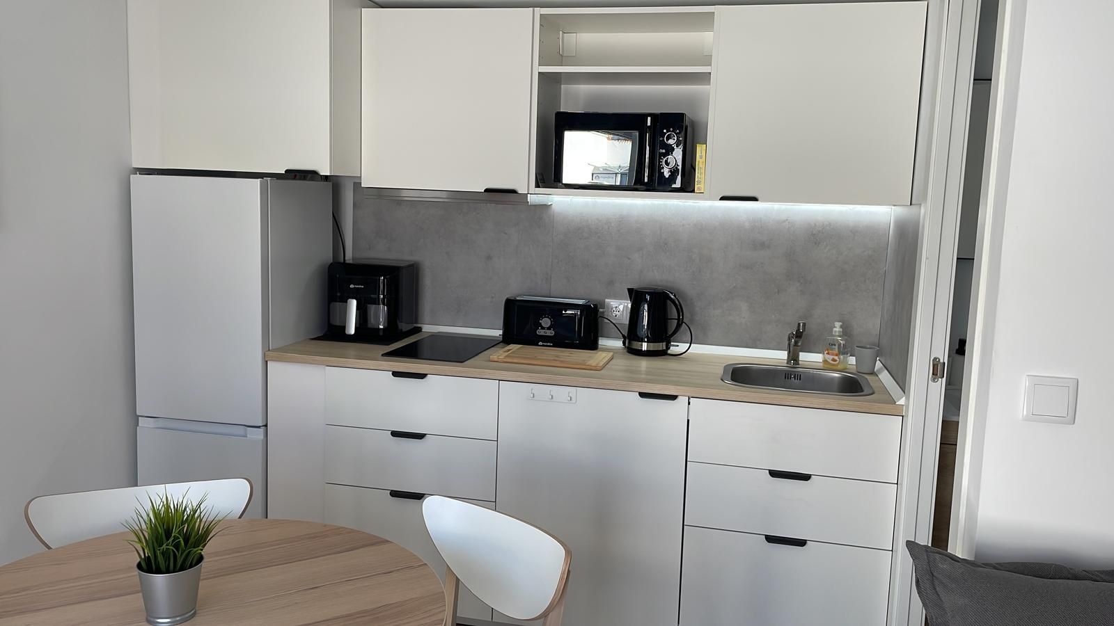 Una pequeña cocina con gabinetes blancos, una mesa y sillas.