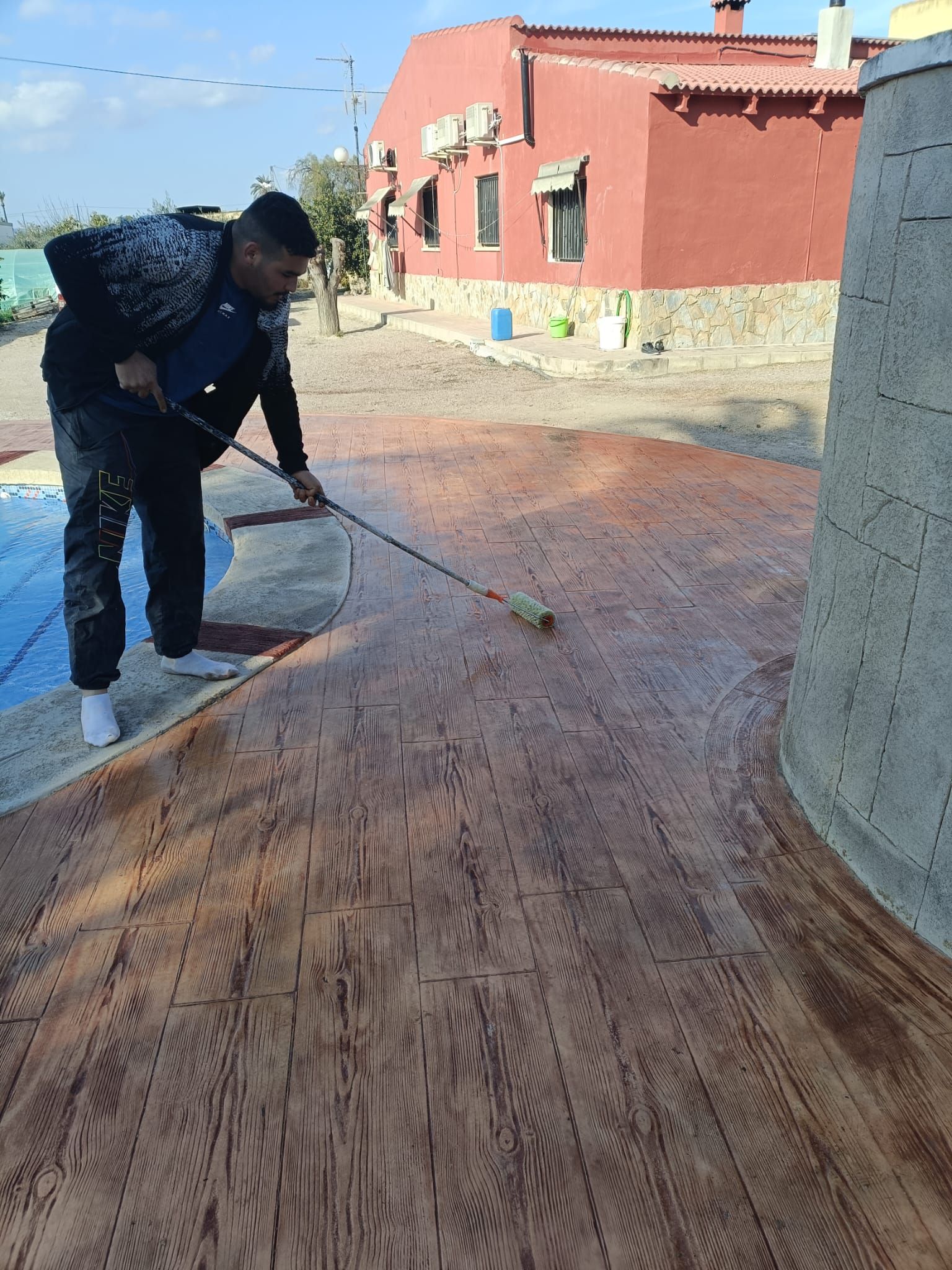 Un hombre está pintando un piso de madera frente a un edificio rojo.