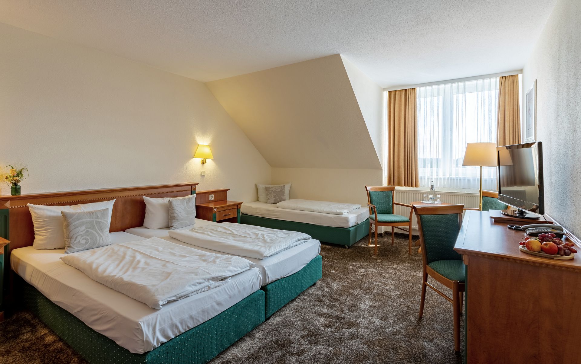 Hotelzimmer mit zwei Betten, Schreibtisch, Fernseher und Fenster mit Vorhängen
