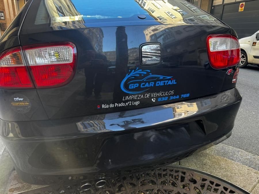 Parte trasera de un sedán negro con una pegatina del concesionario, estacionado en una calle con una rejilla en primer plano.