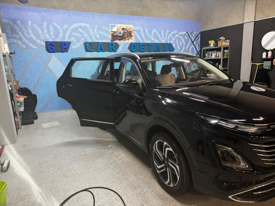 Un SUV negro en un taller de limpieza y detallado de automóviles con la puerta del conductor abierta y un letrero de 