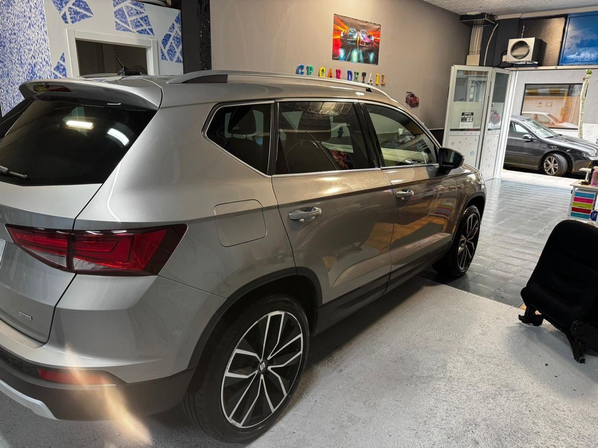 Un SUV plateado estacionado dentro de una sala de exposición con otro vehículo y artículos en exhibición al fondo.