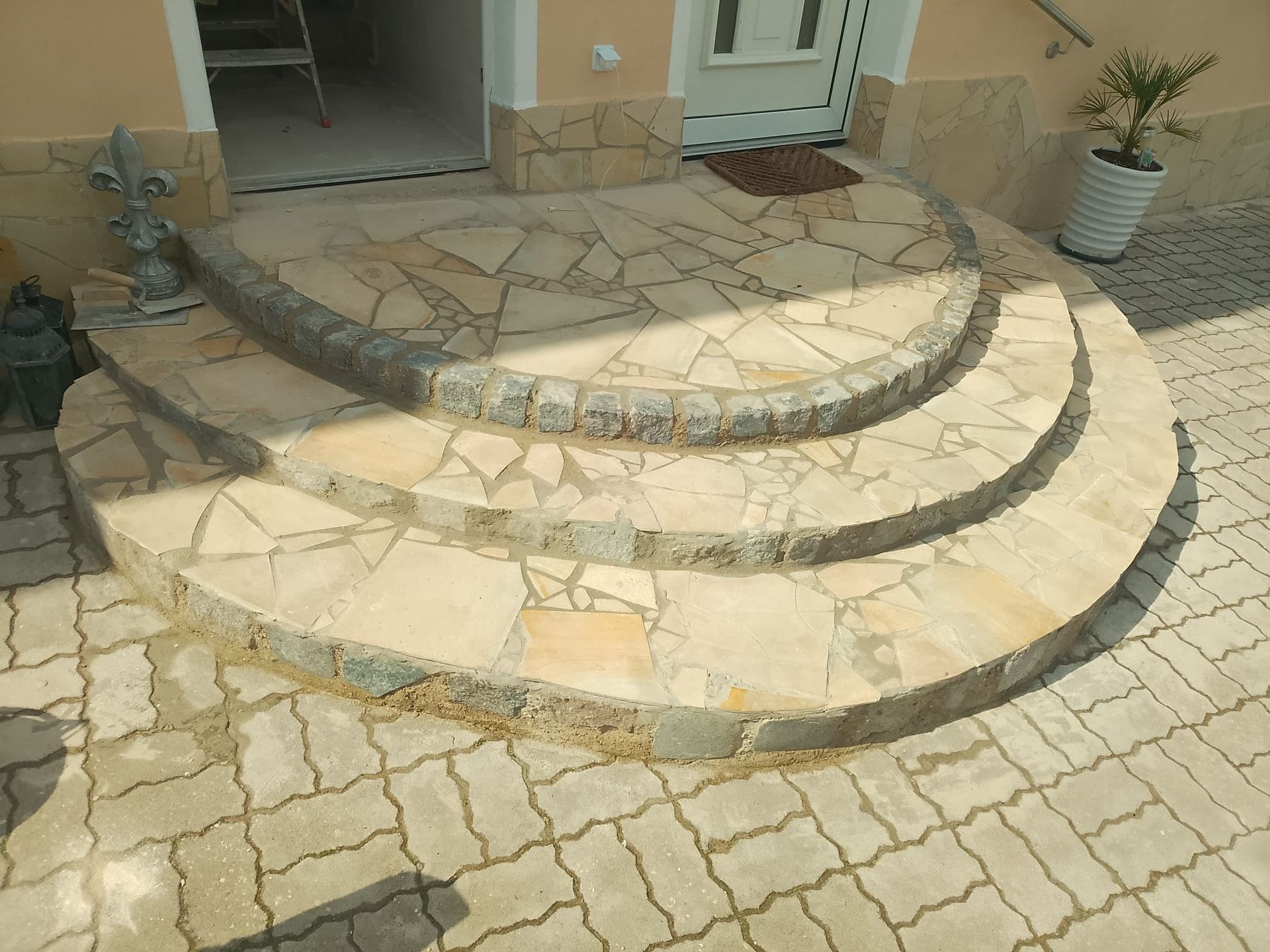 Geschwungene Steinstufen führen zu einem Eingang, gepflasterte Terrasse.