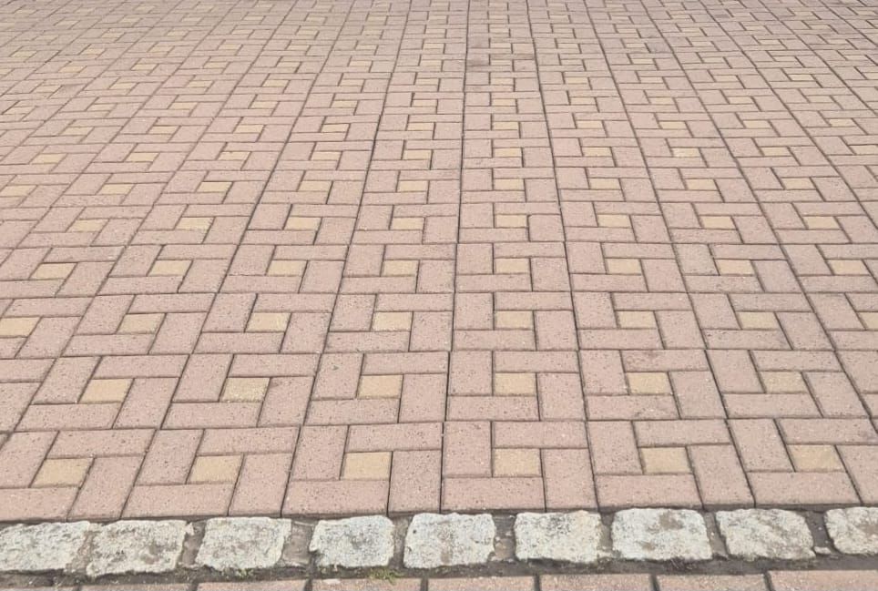 Ein Weg besteht aus Ziegelsteinen, die in einem Flechtmuster verlegt und mit einer Reihe kleiner Steine ​​eingefasst sind.