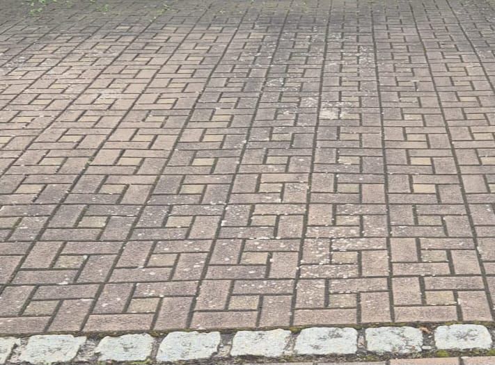 Ziegelterrasse mit sich wiederholendem rechteckigem Muster, verwittert und etwas moosbewachsen.