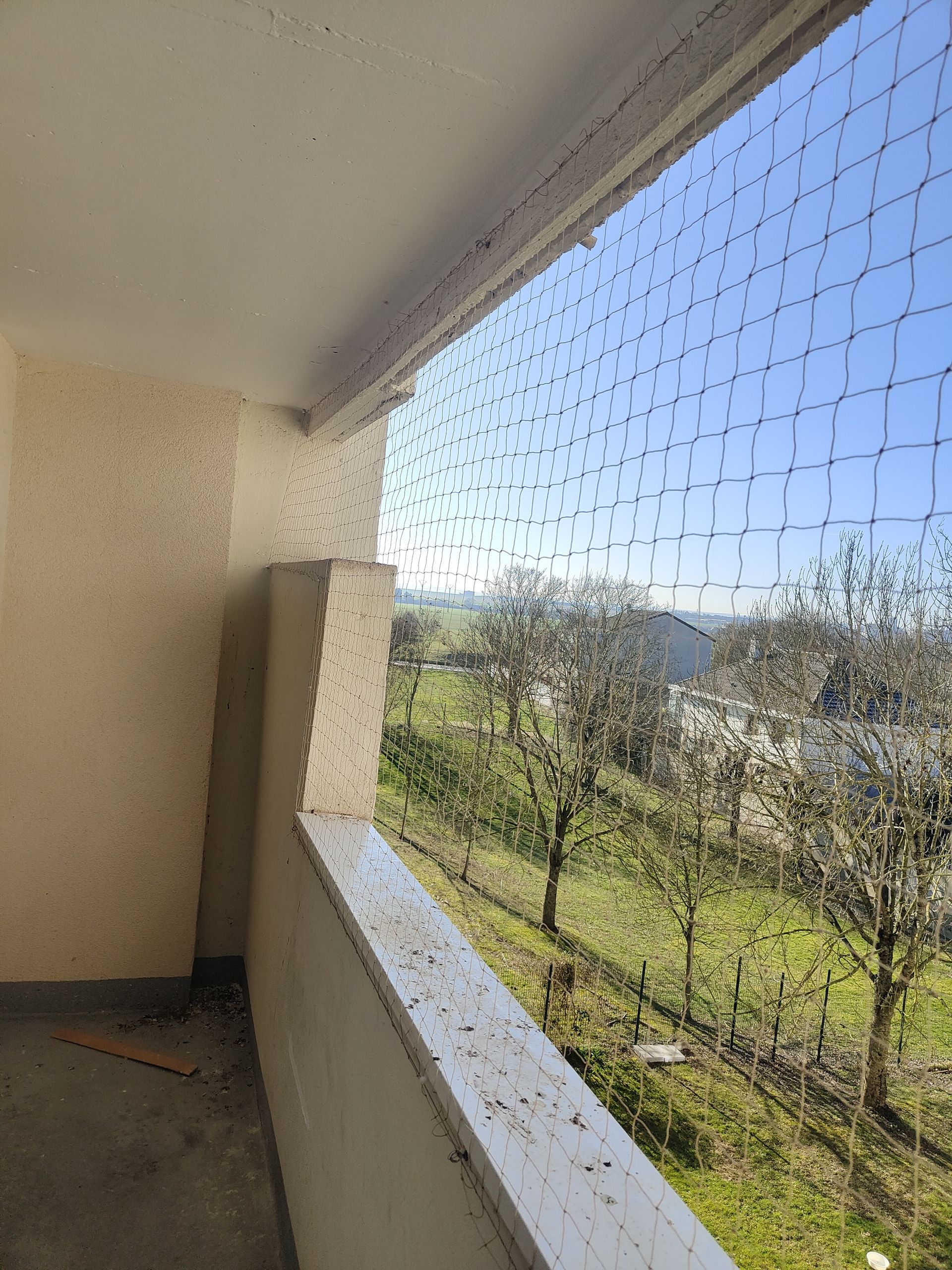 Un balcon avec un filet à oiseaux dessus et une vue sur un champ.