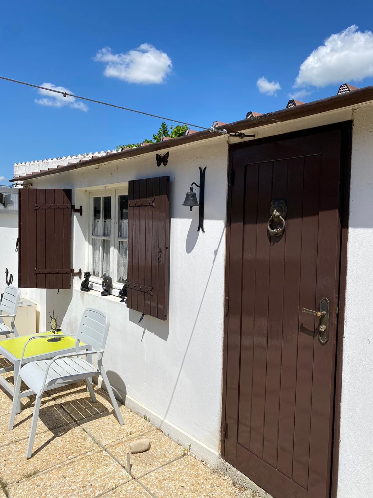 Un bâtiment blanc avec une porte marron et des volets aux fenêtres.